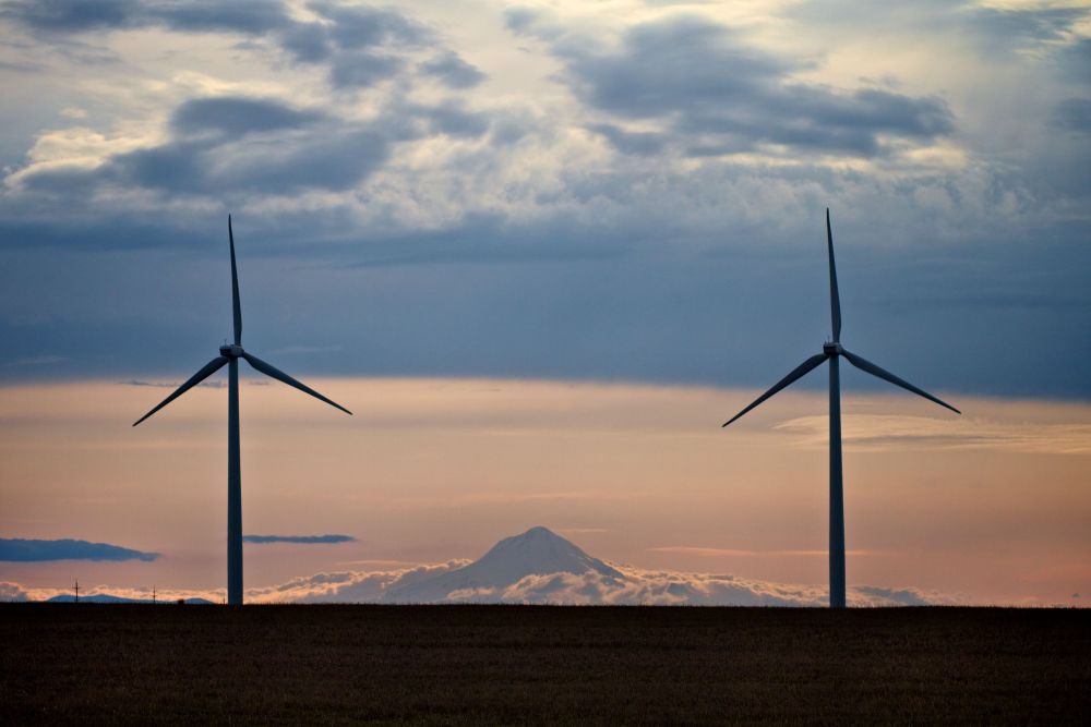 two windmills in front of a sunset against a backdrop of a mountain